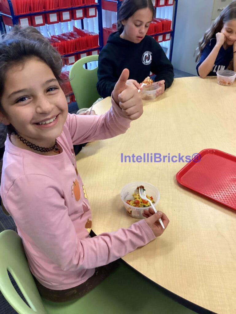 A student giving a thumbs-up while enjoying a healthy snack created during a STEM in the Kitchen summer camp session.