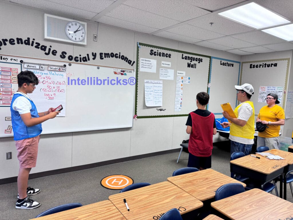 A team of three students and an instructor work together in a classroom to navigate a drone using a mobile controller and flight mission checklists.