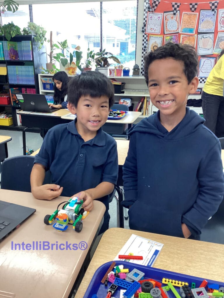 Two smiling students proudly displaying their completed LEGO robotics rover project at a summer STEM camp.