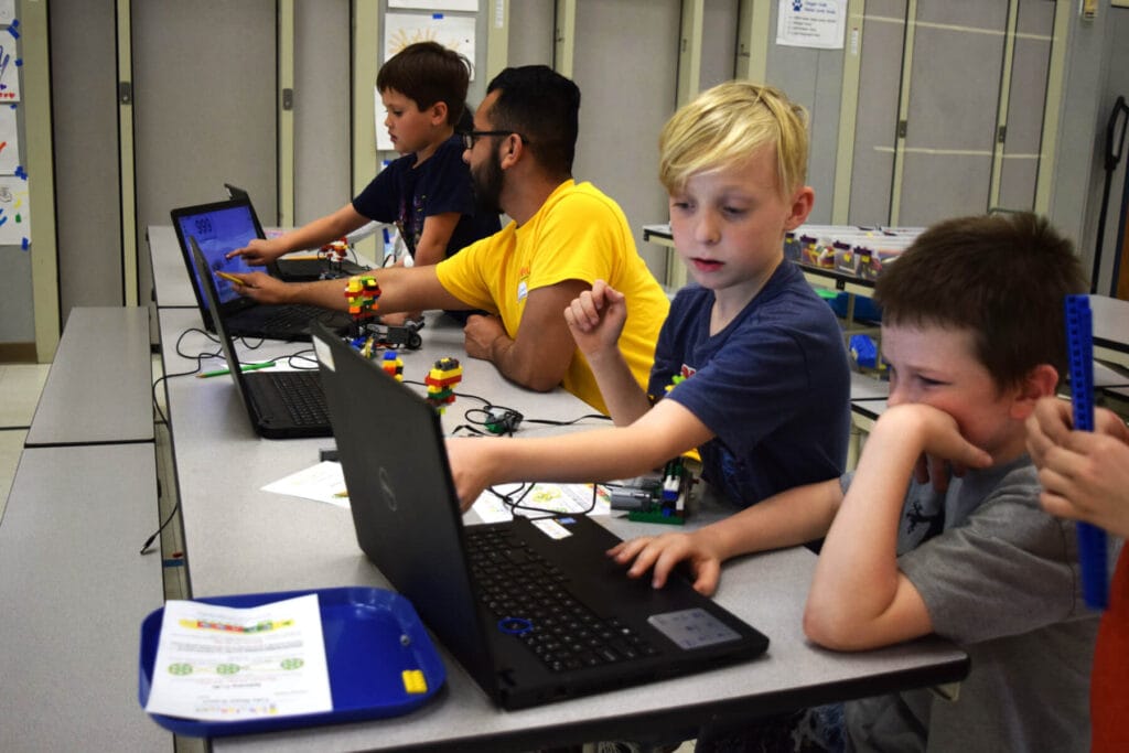 An IntelliBricks STEM instructor providing one-on-one coding guidance to students during a robotics building session.