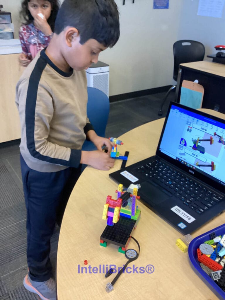 A student building a motorized LEGO engineering project using a laptop with digital design instructions at STEM camp.