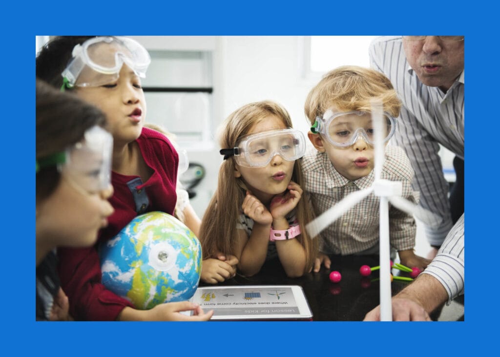 Elementary school students wearing safety goggles blowing on a model wind turbine to learn about renewable energy in an IntelliBricks STEM science class.