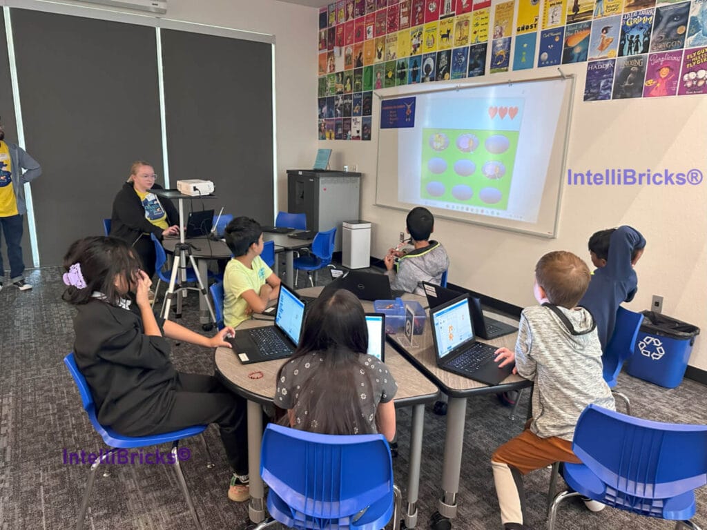 Students at circular tables using laptops to design multi-level arcade games with Scratch coding, building logic flows.