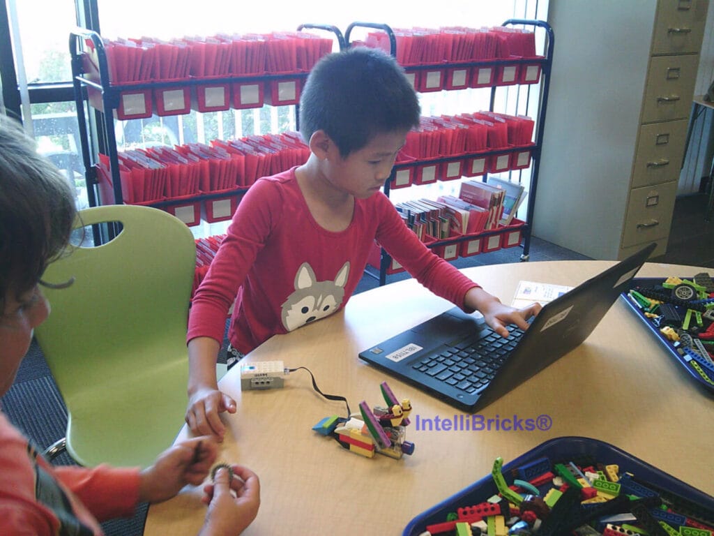 A student using a laptop to program a LEGO robotic creation during a hands-on STEM enrichment class.